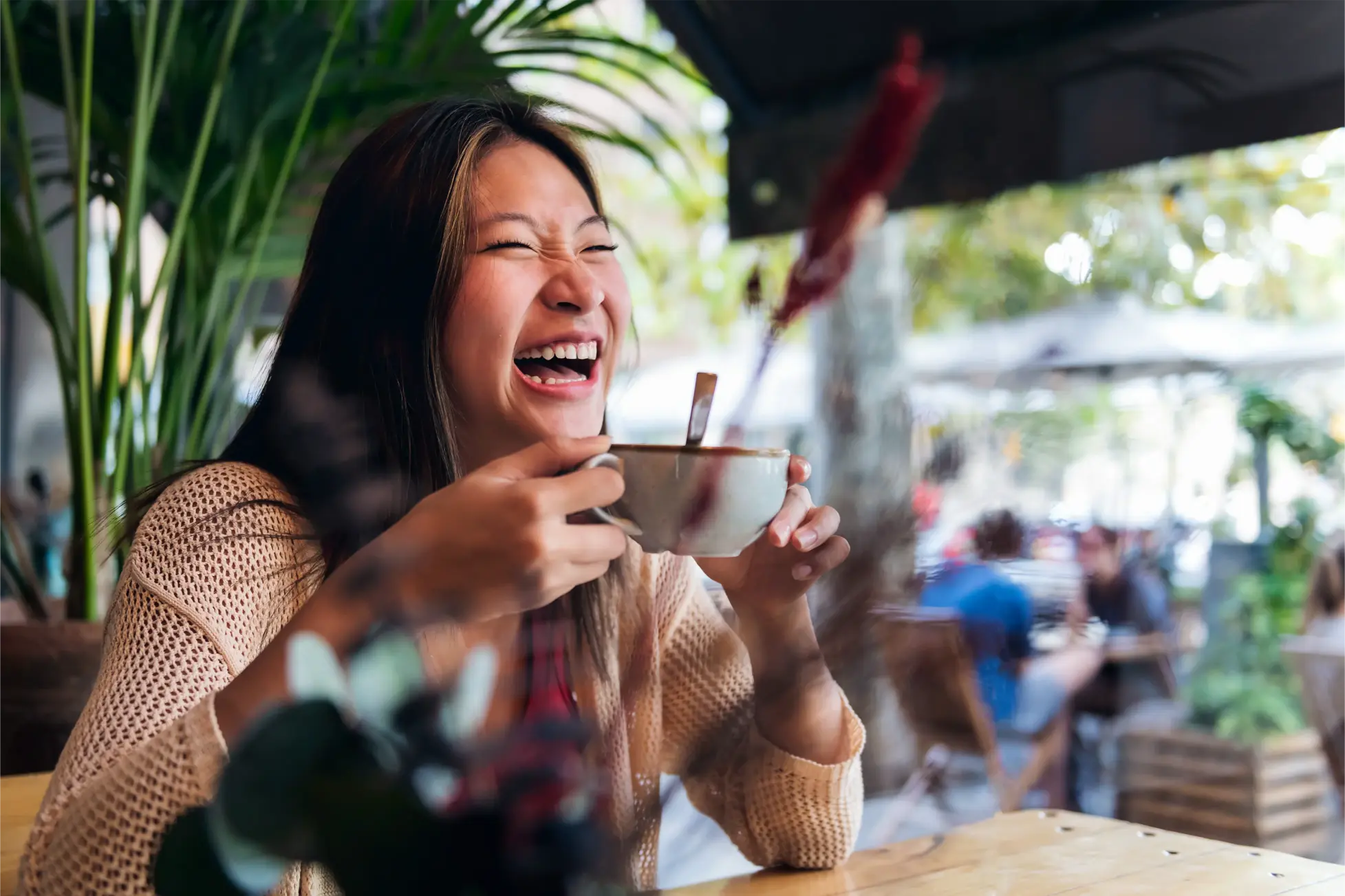 Eine asiatische, lachende Dame trinkt voller Freude ihren Kaffee mit Haferdrink